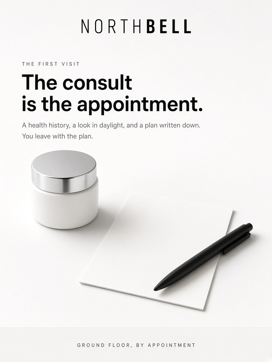 Northbell Aesthetics post: "The consult is the appointment.", a blank white card, a slim black pen and a small white jar on a studio sweep.